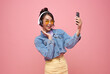 Happy Asian girl listening favourite music playlist on moblie phone application with wireless headphones and dancing isolated on pink studio background.
