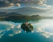 Flying around small island on Bled Lake in Slovenia. Aerial view of Church of the Assumption of Mary in the center of the lake Bled. Warm morning sun and light fog