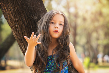 beautiful happy girl playing in the park with blue dress without shoes sitting on tree laughing screaming with happiness in family enjoying children's day