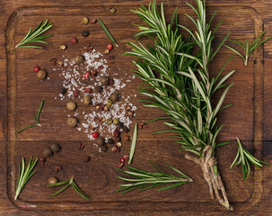 Wall Mural - Twigs and leaves of rosemary, dry fruits of red, black and allspice and salt on a wooden cutting board, top view