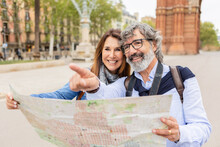 Happy Senior Adult Tourist Couple Holding City Map While Visiting Barcelona On Vacation. Married Middle Aged Man And Woman Looking For Touristic Location Enjoying Summer Holidays Together. Retirement