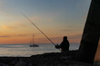 Silhouette of a fisherman with a fishing rod on the seashore at sunset