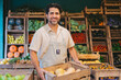 © juanpablo - Middle-aged Latin man with a smile holding a crate of squash in a greengrocer's shop while looking at the camera.