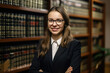 © aicandy - Elegant legal secretary standing in front of a bookcase filled with law books, holding a pen and legal document with a smile, generative ai