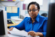 © aicandy - Portrait of a confident and attentive female human services assistant, wearing a blue blouse, while sitting at a desk with a computer and paperwork, generative ai