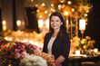 © aicandy - Portrait of a confident event planner with a radiant smile, standing in front of an extravagant event set up with floral arrangements and lighting, generative ai