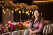 © aicandy - Portrait of a confident event planner with a radiant smile, standing in front of an extravagant event set up with floral arrangements and lighting, generative ai