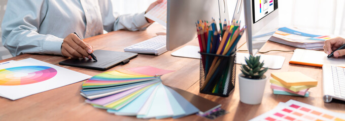 Poster - Graphic designer work on computer laptop and with graphic drawing pen while brainstorming unique design with professional graphic team in modern digital studio workplace. Panorama shot. Scrutinize