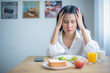 © Digital Art Studio - Beautiful asian girl sat at the table with a stressed expression looking at her breakfast.