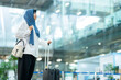 © maya1313 - An Asian Muslim wearing a blue hijab is preparing for a vacation and she is at the airport. She is waiting for her friends, Muslim travelers.