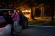 Woman arrives by car to a house in forest, standing with bag and phone near vehicle in the evening time. Traveling by car and rest in cabins on nature concept