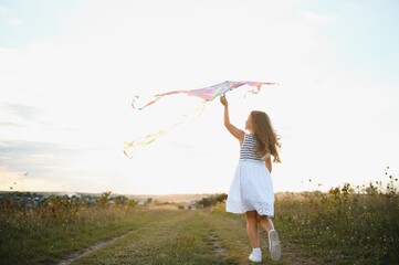 Wall Mural - Little cute 7 years old girl running in the field with kite on summer day