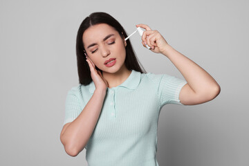 Canvas Print - Young woman using ear spray on light grey background