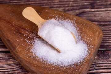 Wall Mural - White refined sugar on wood background. Close-up of granulated sugar in wooden spoon