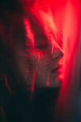 Nightmare dream. Dark consciousness. Red color light defocused tranquil woman face silhouette sleeping with closed eyes covered with distressed polyethylene plastic film.