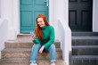 © Westend61 - Happy young woman using smart phone sitting on steps outside house