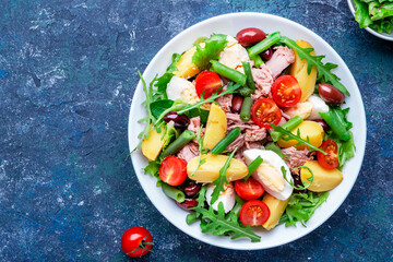 Wall Mural - Nicoise salad with tuna, tomatoes, eggs, green beans, potatoes and olives on plate, blue table background, top view