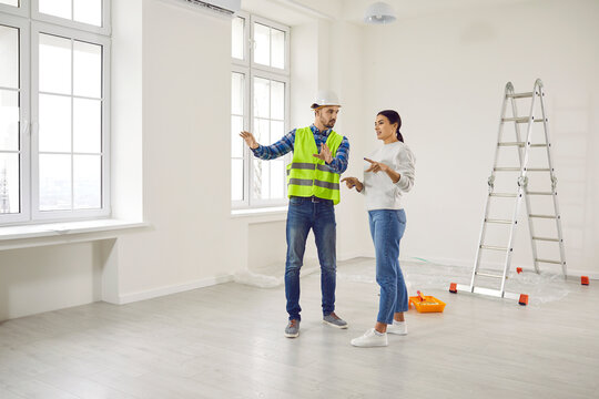 Young woman homeowner discussing design project or repair of her new apartment with foreman standing in empty white room. Meeting with builder about interior decoration or home layout. Moving concept.