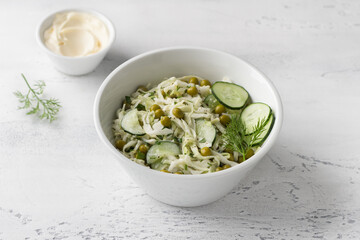 Wall Mural - Salad with white cabbage, green peas, cucumber, herbs and mayonnaise sauce on a light blue background