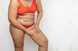 © Юля Бурмистрова - Overweight woman bending over massage hip with hands, white background. Naked woman in red underwear with hanging belly and fat body. Weight loss, anticellulite treatment, plus size people.
