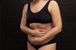 © Юля Бурмистрова - Plus size woman in black underwear covering with hands hanging belly. Hide figure imperfections, fat body. Studio portrait over black background. Concept of obesity, body positive, self acceptance.