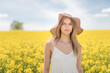 Beautiful woman with long blonde hair wearing a hat. He walks in the rapeseed field