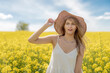 Beautiful woman with long blonde hair wearing a hat. He walks in the rapeseed field