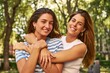 © Asier - Two friends embrace and smile in a park.