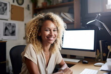 Generative AI illustration of cheerful young African American female freelancer with Afro hairstyle smiling and looking at camera while sitting at wooden table during work on remote project on laptop