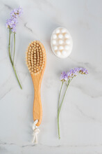 Full Body Dry Massage Brush And Handmade Honey Soap From Above On Marble Background With Purple Flowers