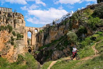 nice, active senior woman riding her electric mountain bike below the famous new bridge of ronda, an