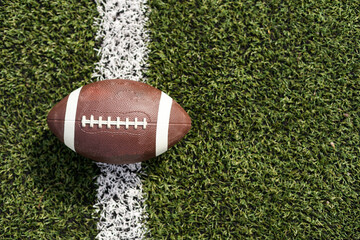 Photo of a rugby ball on a grass next to the white line, shot from above