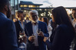 Diverse business people of different ages and races, having a business cocktail on a terrace in the evening. Generative AI