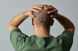 © Seventyfour - Back view of mature bald man touching head against pale grey background