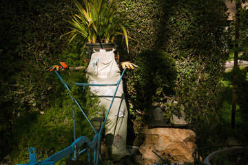 Scarecrow stands in garden tall in its eco-friendly attire apron, colored gloves, and a green plant pot for a head. A symbol of sustainable living, ecology, recycle, sustainability, reusing, concept.