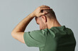 © Seventyfour - Side view of mature bald man touching head against pale grey background