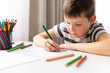 © spyrakot - A child boy draws on white paper with colored pencils while sitting at a table