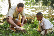 © Seventyfour - Full length portrait of adult scout leader teching little boy start campfire in forest