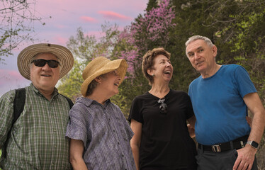 older friends talking and laughing in midwestern park; woody river bluffs with blooming redbud trees