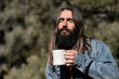 © Lauren Justice/Stocksy - Man with long hair on porch in nature with coffee