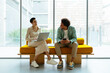 © BONNINSTUDIO/Stocksy - Coworkers discussing project sitting on yellow sofa in a workspace
