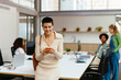 © BONNINSTUDIO/Stocksy - Cheerful woman using smartphone in office