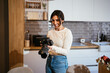 © Manu Padilla/Stocksy - Happy woman with photo camera in kitchen