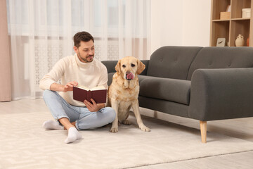 Poster - Man reading book on floor near his cute Labrador Retriever at home