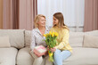 © New Africa - Young daughter congratulating her mom with flowers and gift at home. Happy Mother's Day