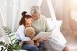 © Pixel-Shot - Little girl with toy and her grandmother reading book in bedroom