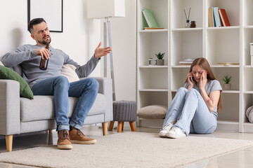 Wall Mural - Bruised young woman talking by mobile phone and her drunk husband at home. Domestic violence concept