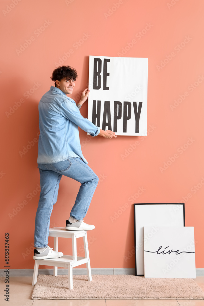 Young man hanging poster on pink wall
