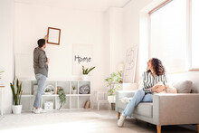Young Couple Hanging Blank Frame On Light Wall At Home
