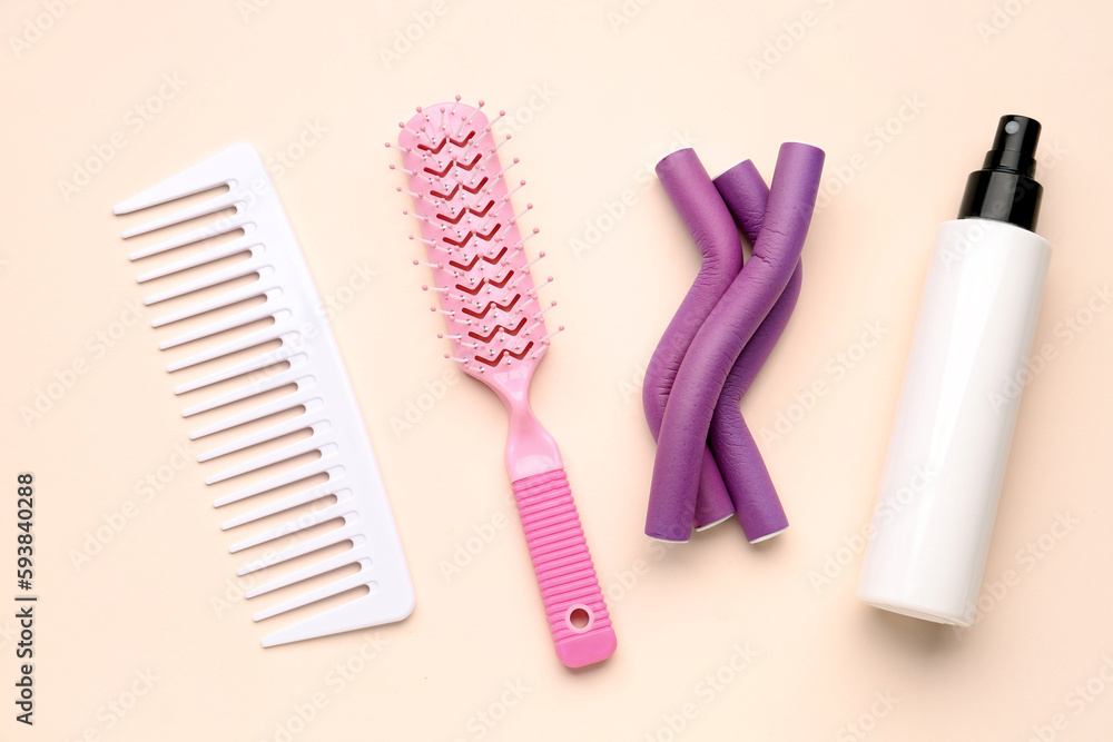 Hair brushes with curlers and spray bottle on beige background